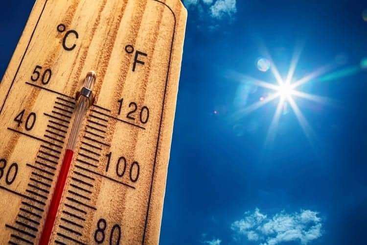A wooden thermometer shows high temperatures in both Celsius and Fahrenheit, with the sun shining brightly in a clear blue sky.