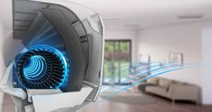Close-up of an air conditioner emitting cool air in a modern living room with a sofa and large window in the background.