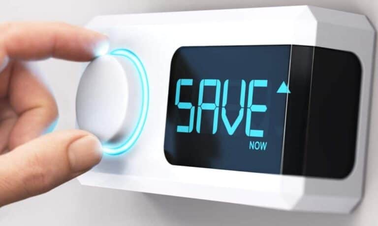 A hand adjusts a digital thermostat displaying the word "SAVE" in blue letters, indicating energy-saving mode.