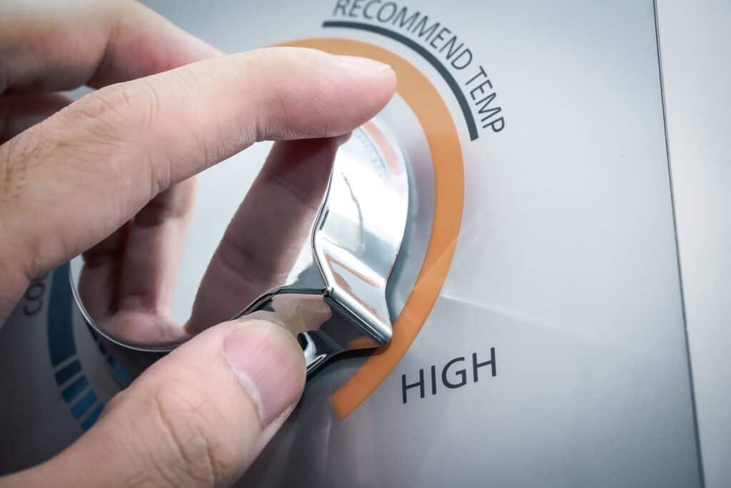 A hand turns a metallic dial on a control panel, setting it to the "High" temperature option.