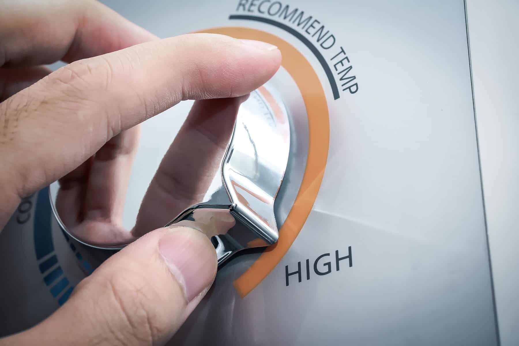 A hand turns a metallic dial on a control panel, setting it to the "High" temperature option.