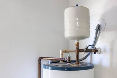 A residential water heater with connected pipes and an expansion tank is installed against a white wall.