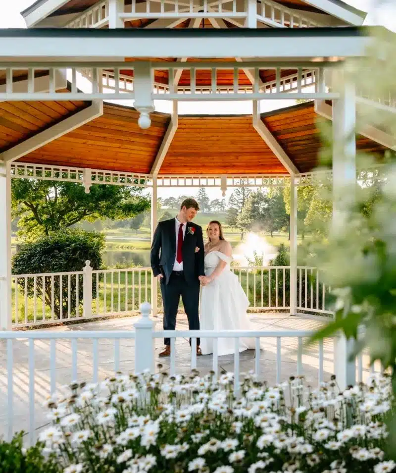 Wedding couple at Cascades Manor gazebo, surrounded by lush greenery and water views.