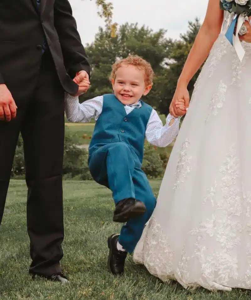 Child happily jumping while holding hands with adults at Cascades Manor wedding.