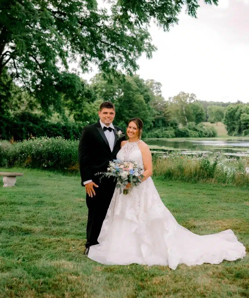Wedding couple in formal attire at Cascades Manor with lush greenery and lake backdrop.