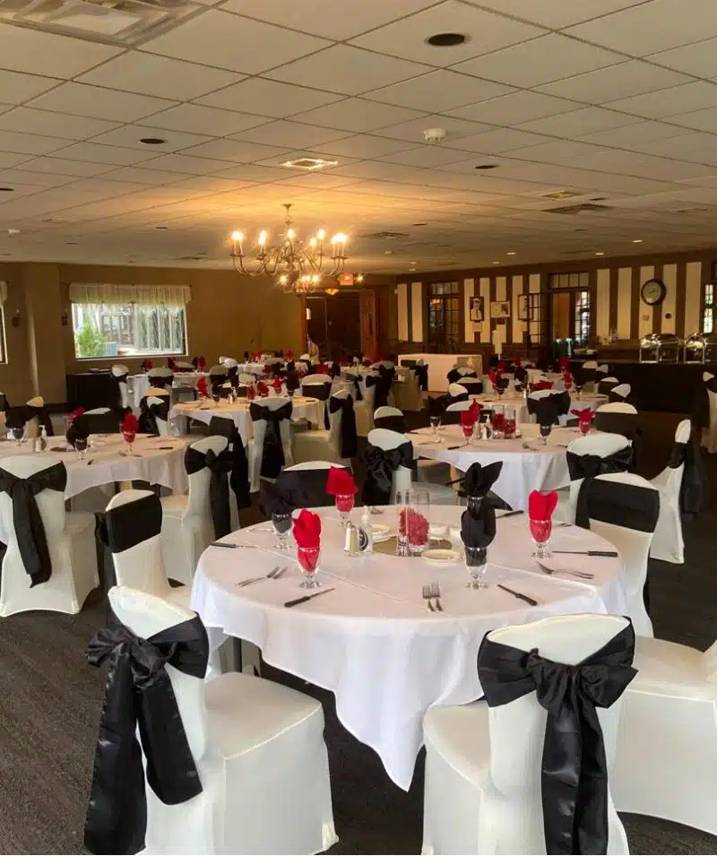 Event hall setup with round tables, white tablecloths, and black chair sashes at Cascades Manor.