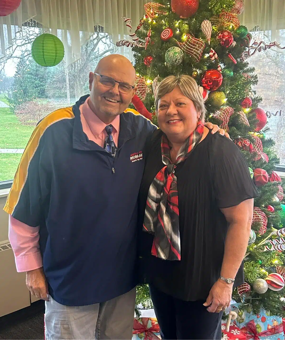 Festive holiday celebration with two smiling people in front of a decorated Christmas tree at Cascad.