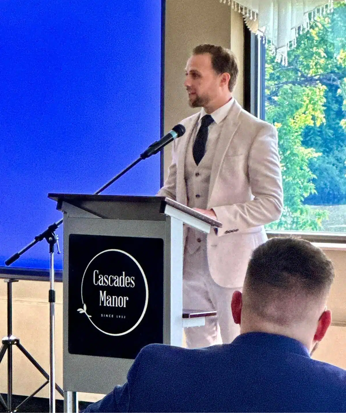 Man giving speech at Cascades Manor conference or wedding event.