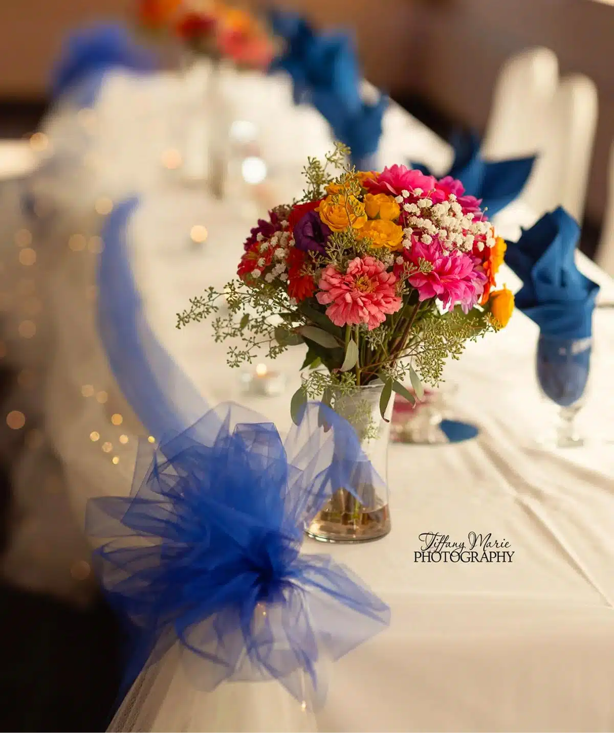 Floral centerpiece with colorful flowers and blue tulle at Cascades Manor event.