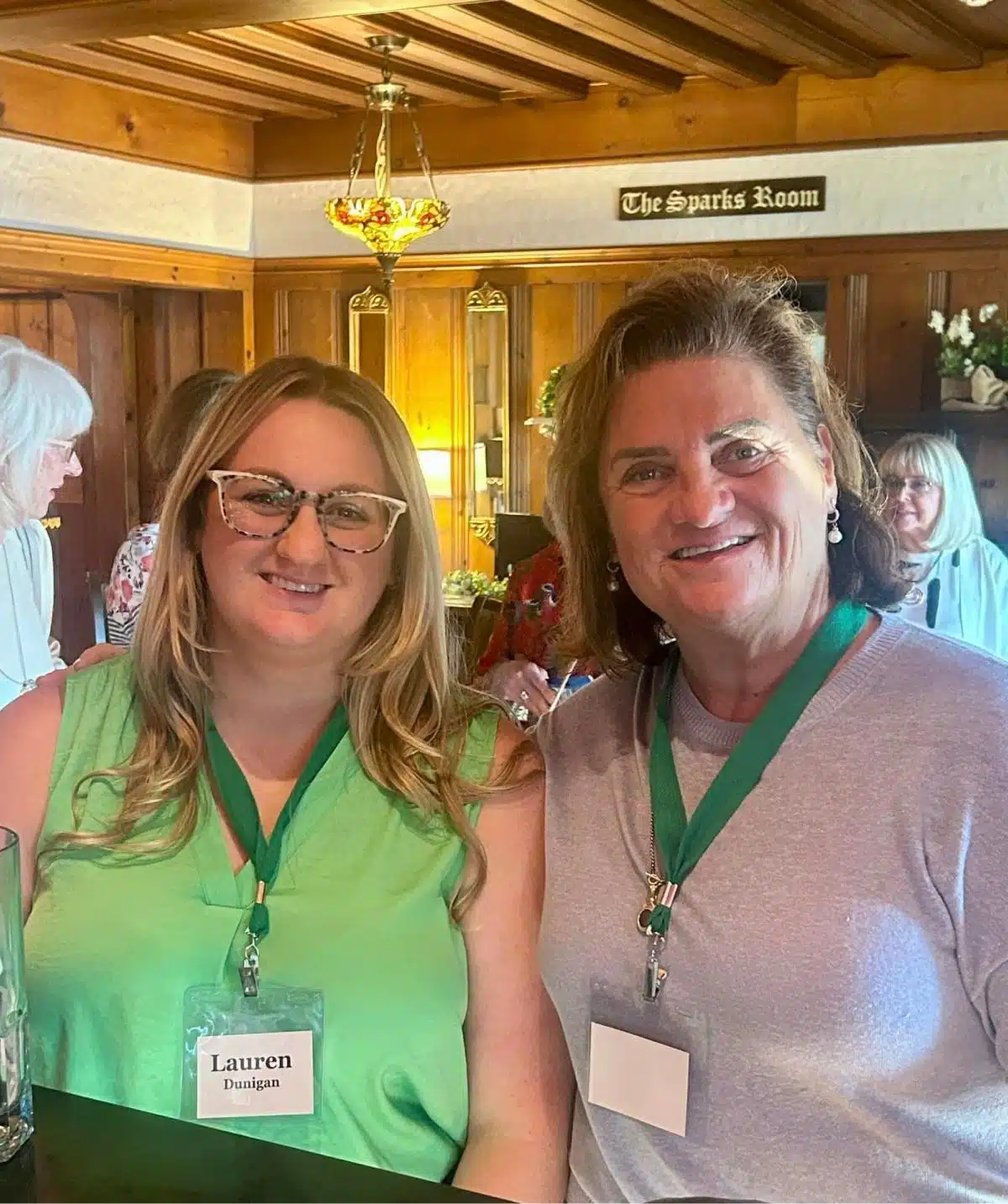 Smiling women at Cascades Manor event in a warm, wood-paneled room.