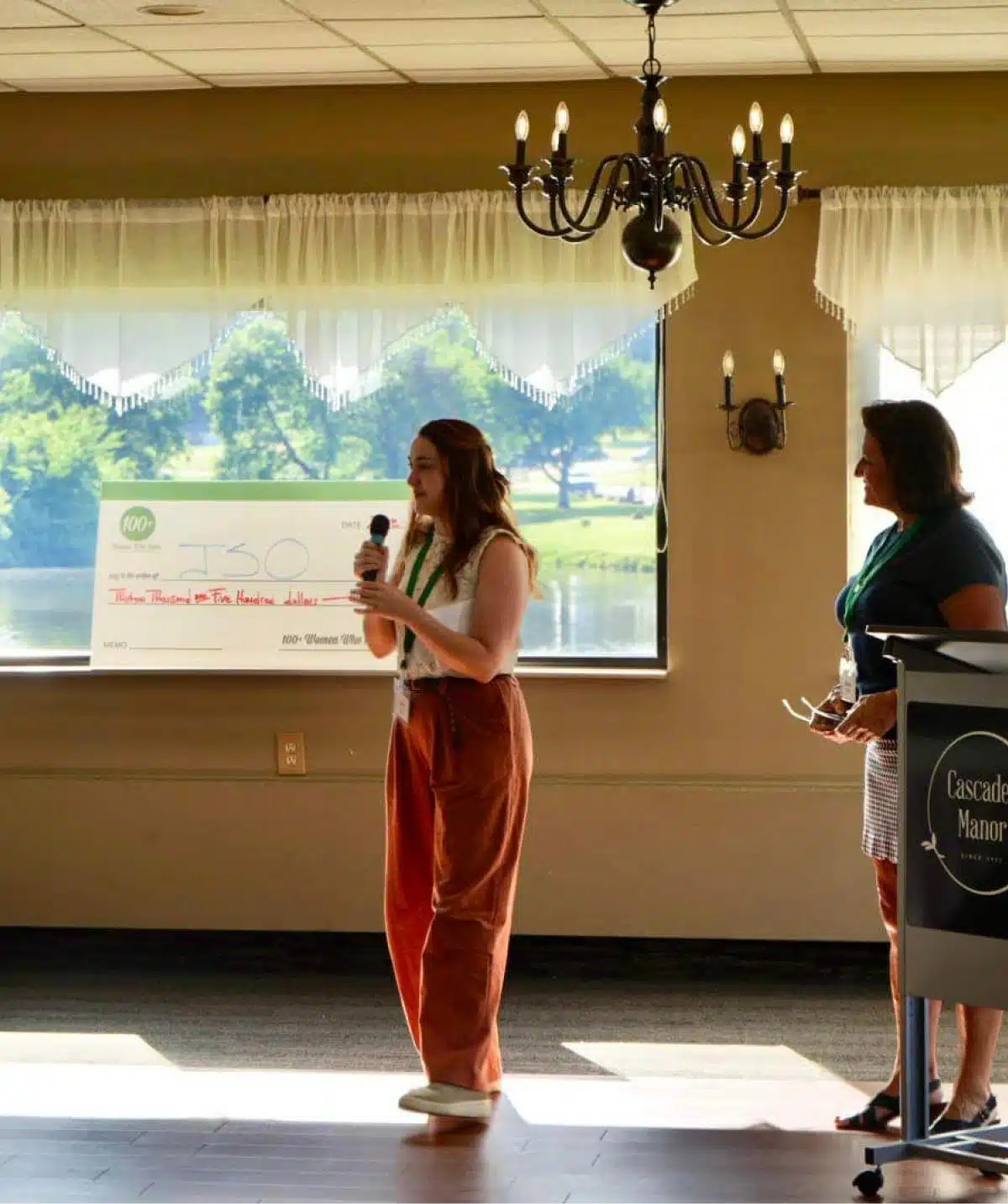 Woman speaking at Cascades Manor event with presentation screen behind.