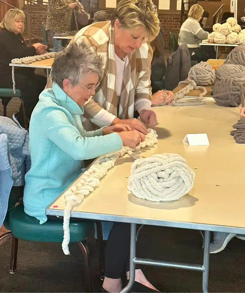 Women knitting large yarn projects at Cascades Manor community event.