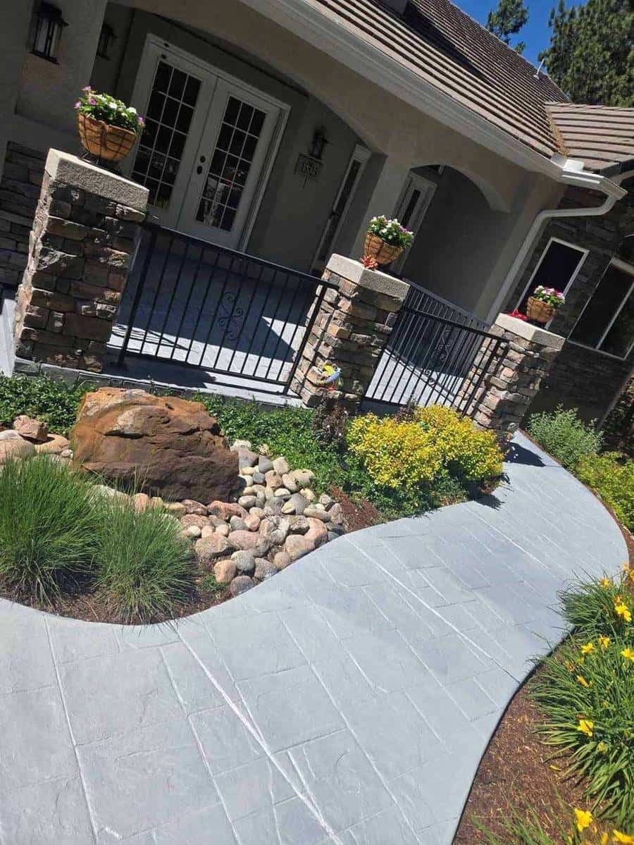 Light‑gray stamped concrete walkway with decorative border and rock garden beside a porch