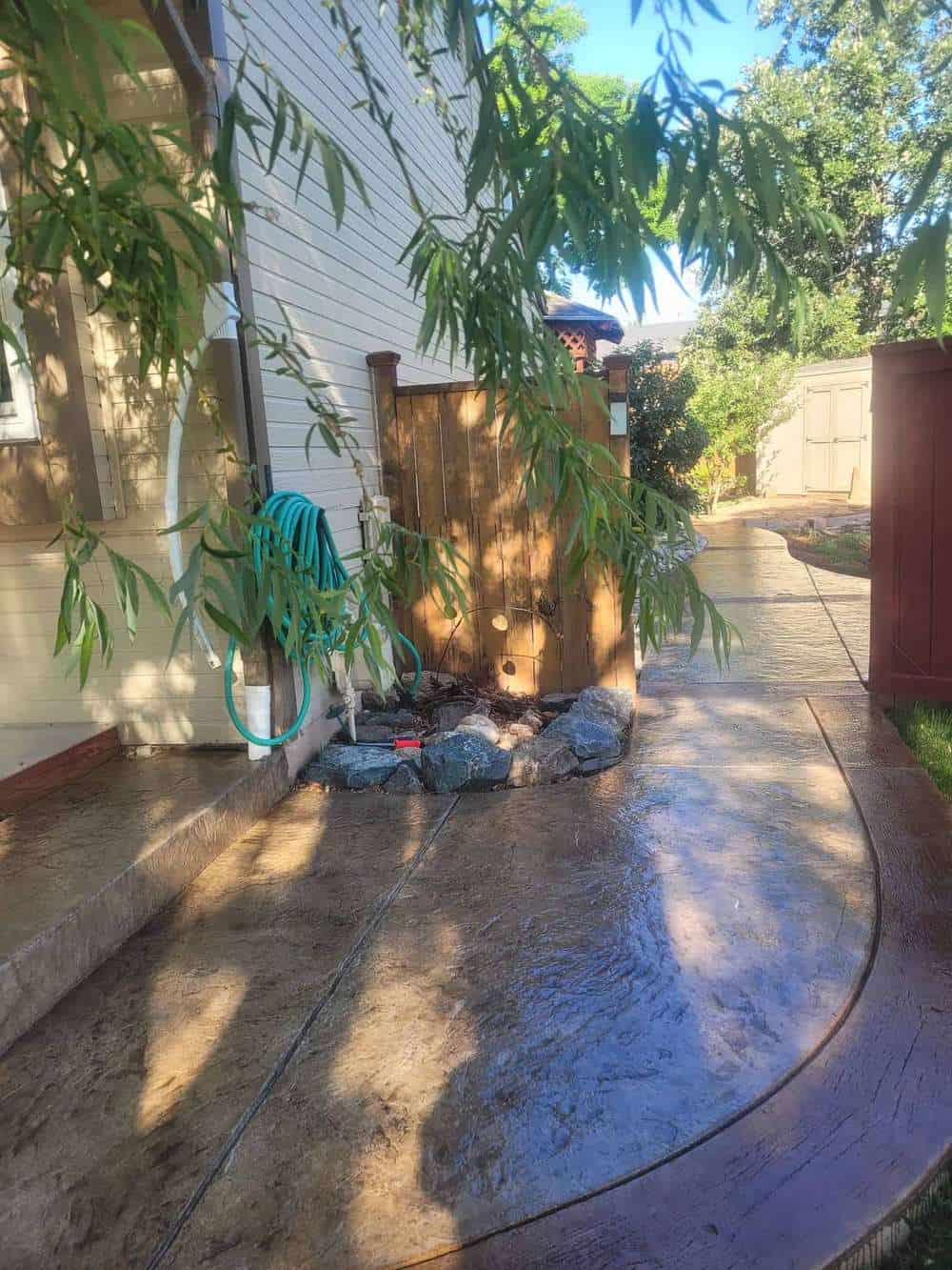 Curved stamped concrete walkway with dark broom‑finish border and wet‑seal sheen in a Colorado Springs backyard
