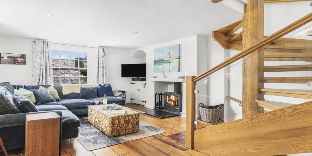 Cozy living room in Cornish Secrets cottage with fireplace and wooden staircase, seaside decor, perfect for relaxing Cornwall holidays.
