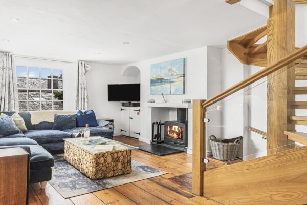 Cozy living room in Cornish Secrets cottage with fireplace and wooden staircase, seaside decor, perfect for relaxing Cornwall holidays.