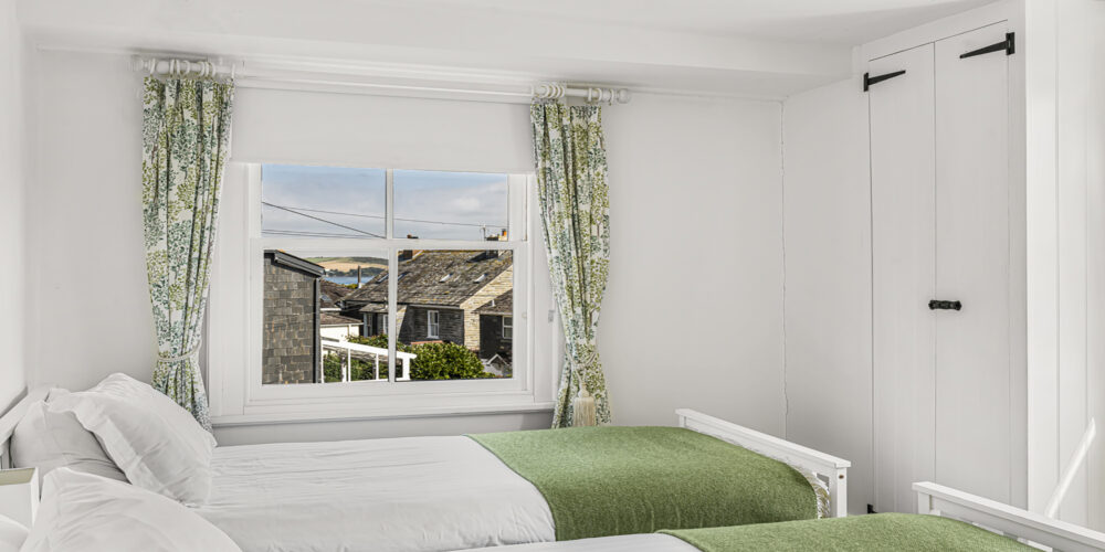 Coastal bedroom with white walls, green bedding, and ocean views from a large window.