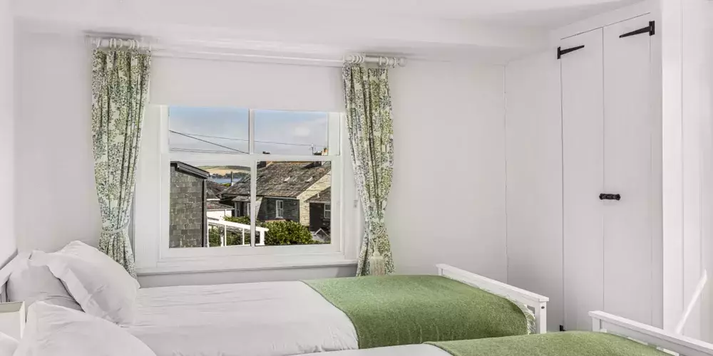 Coastal bedroom with white walls, green bedding, and ocean views from a large window.