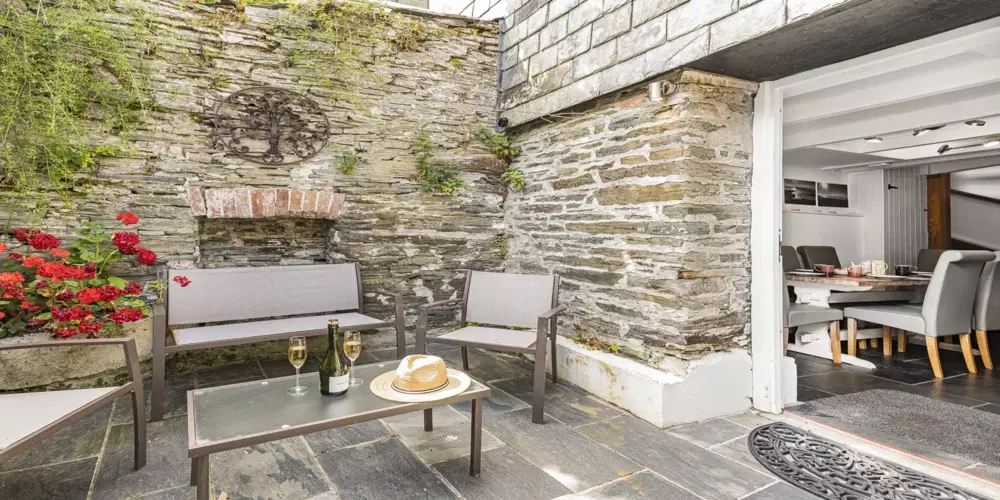 Cozy Cornwall holiday cottage outdoor seating area with stone walls and floral accents.