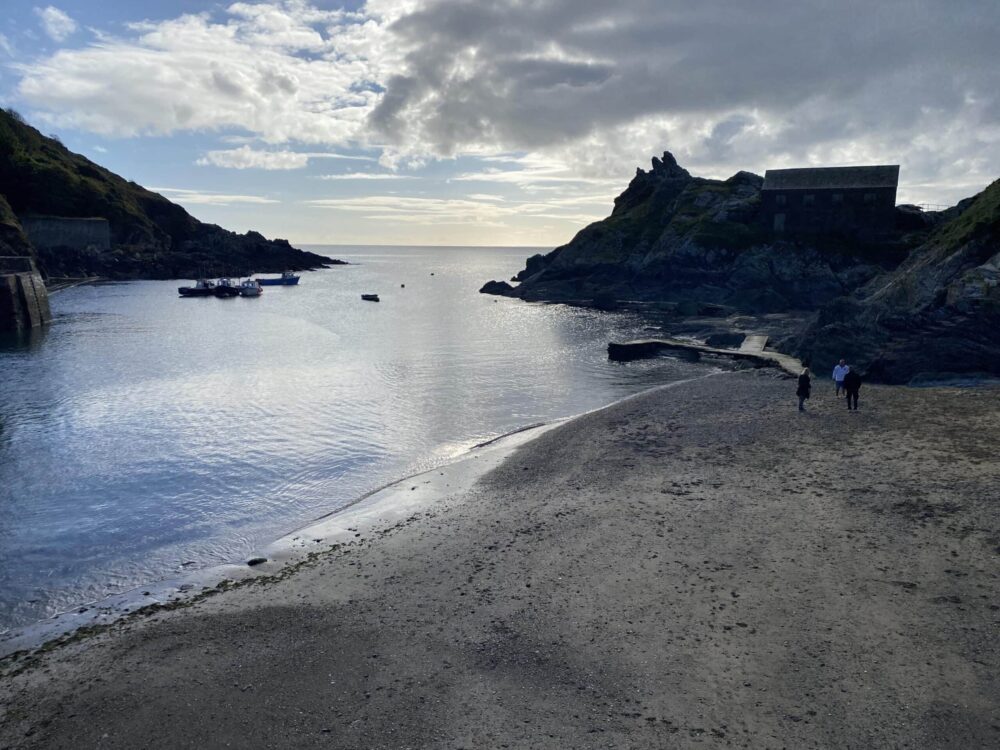 Seaside cove with boats and dramatic cliffs in Cornwall, ideal for coastal holidays.
