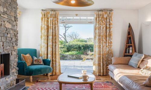 Cozy living room with stone fireplace, colourful seating, and large patio doors opening to garden.