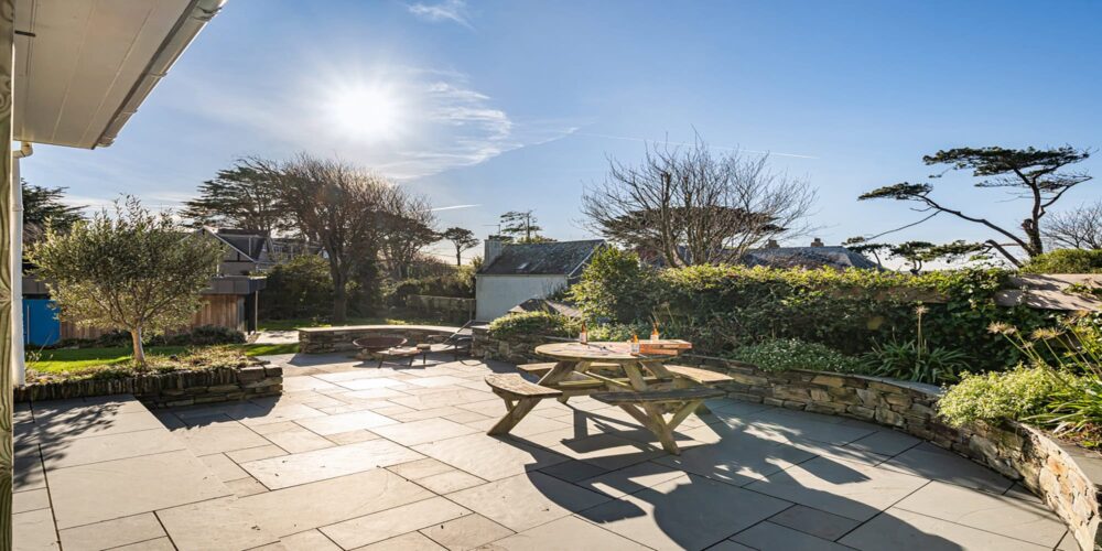 Sunny outdoor patio with garden seating, overlooking lush greenery in Cornwall.