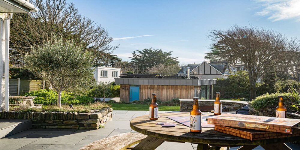 Relaxing outdoor garden at Cornish Secrets with beer bottles, patio table, and scenic trees.