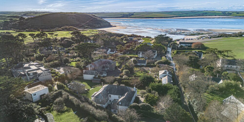 Panoramic aerial view of Cornish seaside village near the coast, featuring lush greenery, charming houses, and sandy beaches.
