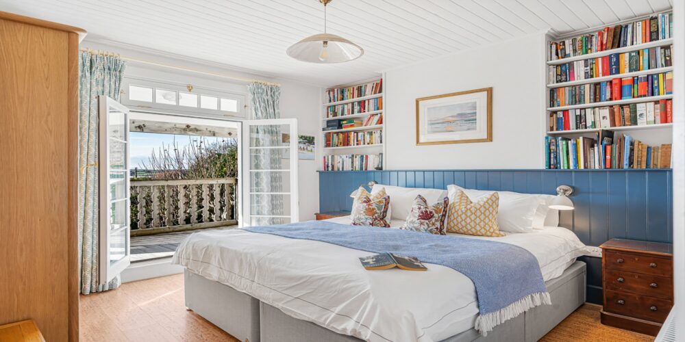 Coastal bedroom with sea view, bookshelf, and cosy decor at Cornish Secrets holiday cottage in Cornwall.
