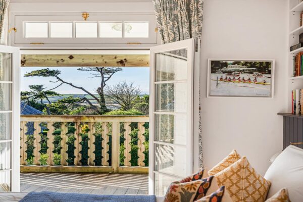 Bright bedroom with open doors leading to a seaside balcony, featuring scenic ocean views and lush greenery.