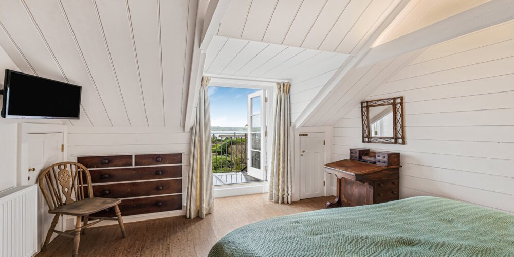 Traditional Cornish cottage bedroom with sea view, rustic furniture, and cosy decor, perfect for a relaxing stay.