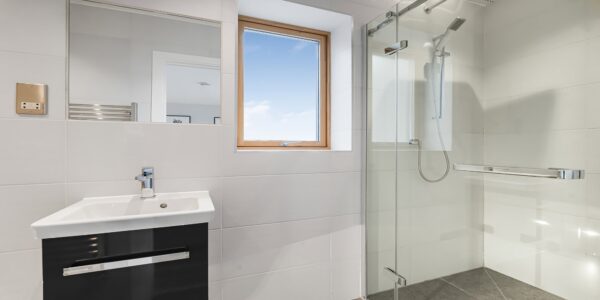 Modern bathroom with walk-in shower and white tiles, natural light from window, stylish and clean design.