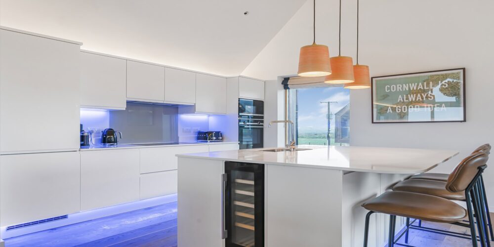 Modern white kitchen with blue LED lighting, open view, and stylish bar stools, Cornish Secrets.