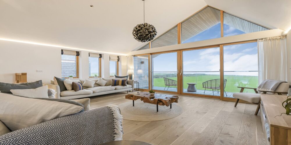 Stunning modern living room with large glass windows overlooking scenic Cornish countryside.