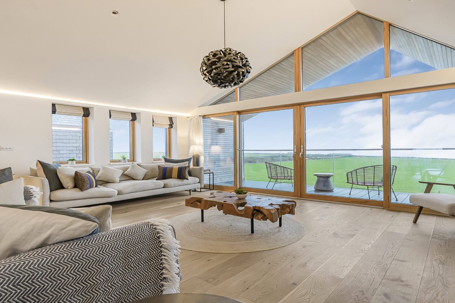 Stunning modern living room with large glass windows overlooking scenic Cornish countryside.