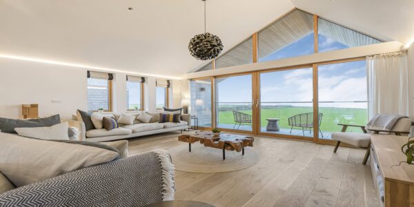 Stunning modern living room with large glass windows overlooking scenic Cornish countryside.
