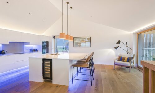 Bright modern kitchen with white cabinetry and wooden accents, stylish seating, and scenic view of Cornwall.