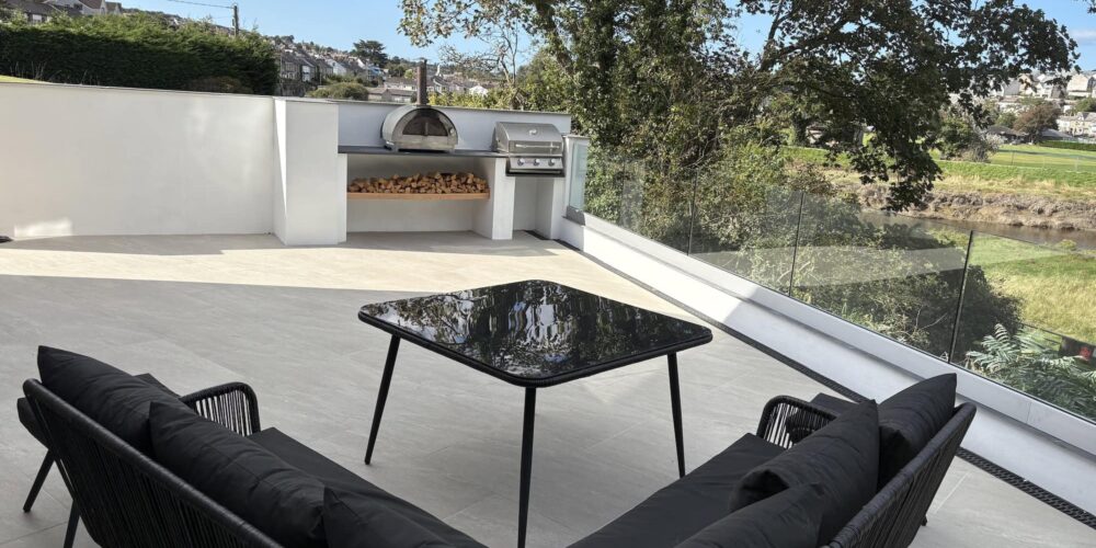 Stunning outdoor terrace featuring modern black furniture, built-in BBQ, and scenic river views in Cornwall.