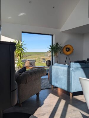 Bright living room with large window overlooking Cornish countryside, stylish furniture and modern decor.