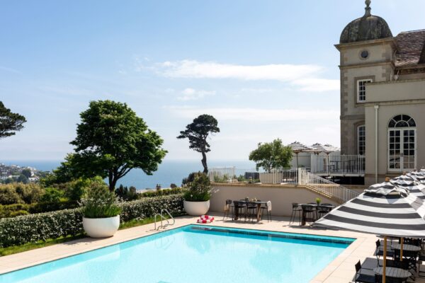 Poolside view at Cornish Secrets with lush greenery and scenic coastal backdrop.