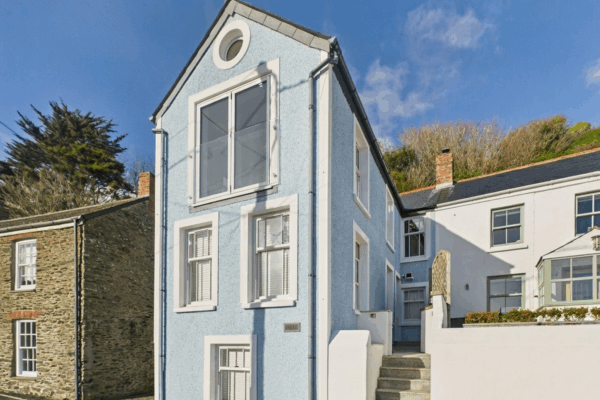 Charming blue coastal cottage in Cornwall with white window frames and stairs.