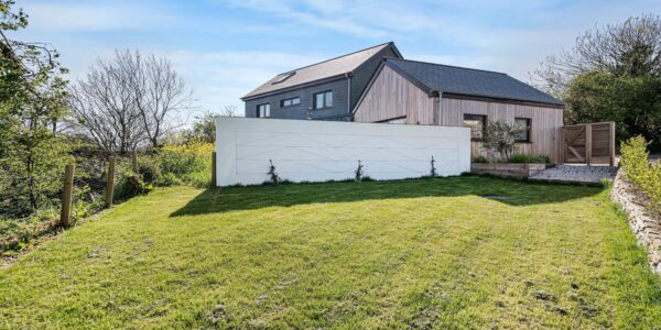 Tranquil countryside retreat at Cornish Secrets with lush green lawn and modern barn-style accommoda.