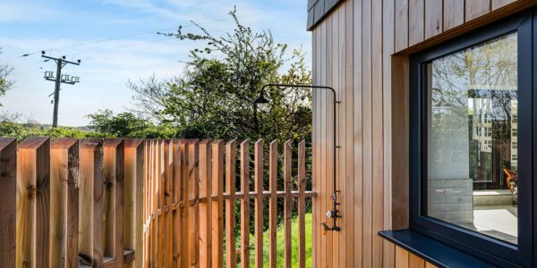 Wooden exterior of Cornish Secrets with garden and fence.