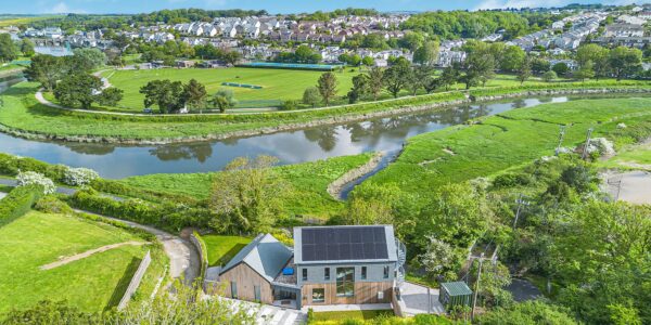 Countryside and river scene with lush greenery and a modern house in Cornwall.