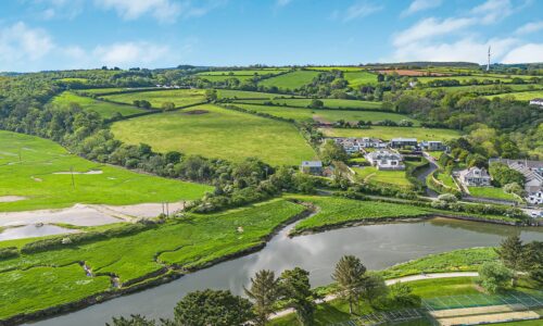 Scenic view of lush green fields, a river, and rolling hills in Cornwall, showcasing the natural bea.