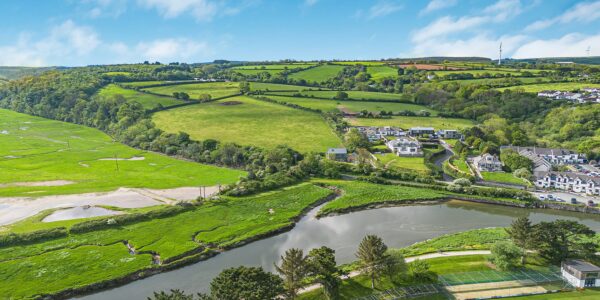 Scenic view of lush green fields, a river, and rolling hills in Cornwall, showcasing the natural bea.