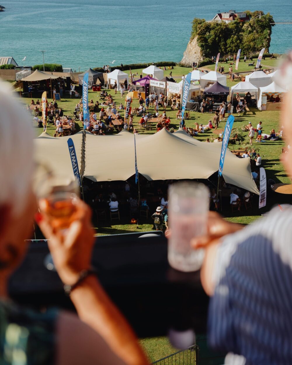 Crowd enjoying outdoor festival with tents and seaside view in Cornwall.