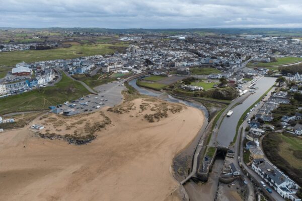 Aerial view of a coastal town in Cornwall with beaches, river, and residential areas.