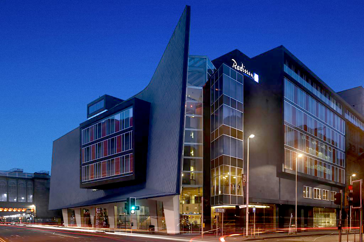 Futuristic hotel building with illuminated glass facade at dusk, showcasing modern architecture.