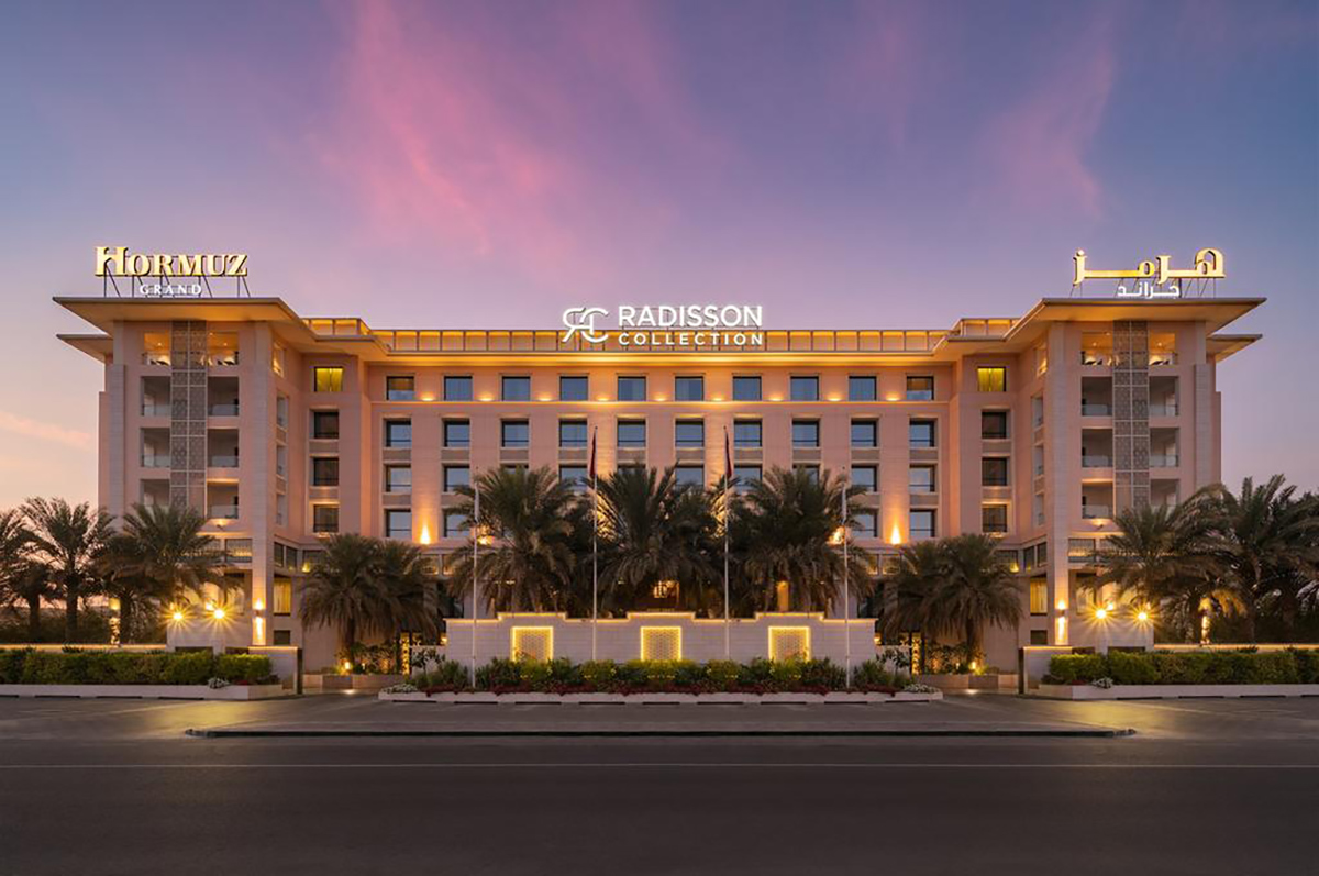 Modern hotel building at night with illuminated signs and palm trees, Radisson Collection logo clearly visible.